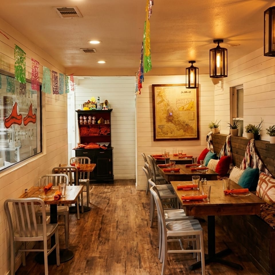 Cozy restaurant interior with wooden tables, cushioned bench seating, and colorful decorations under warm lighting.