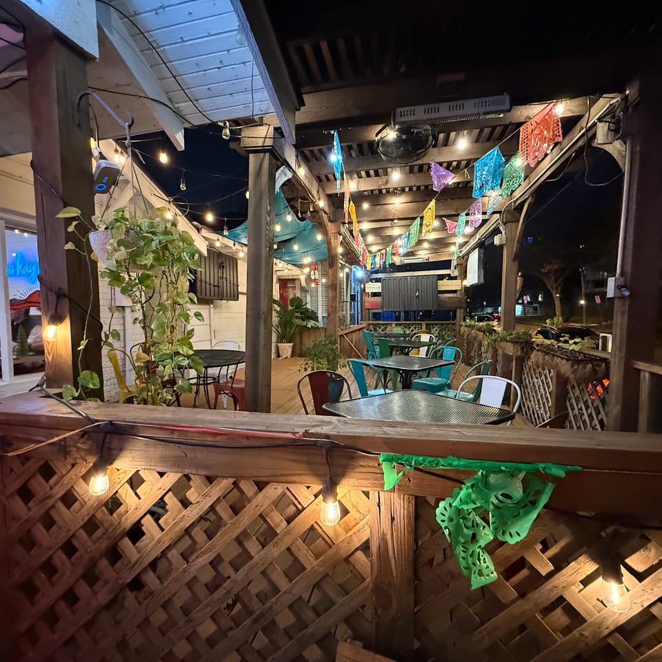 Outdoor restaurant patio at night, illuminated by string lights and colorful papel picado banners.