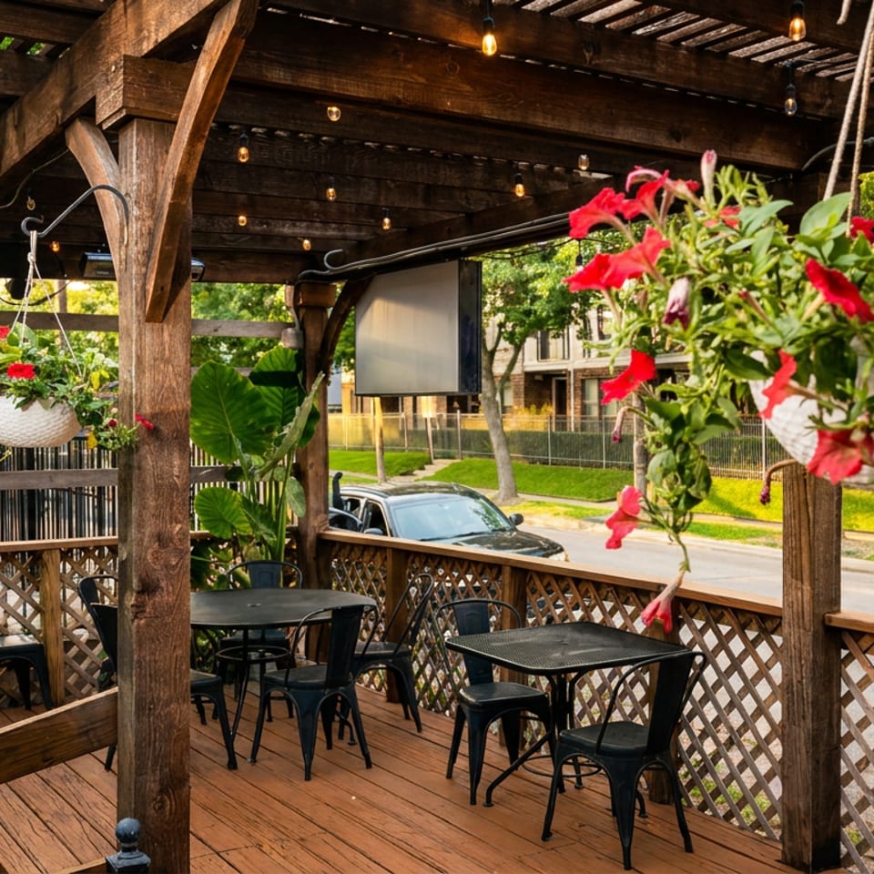 Outdoor restaurant patio with wooden pergola, black tables and chairs, and hanging red flower baskets.