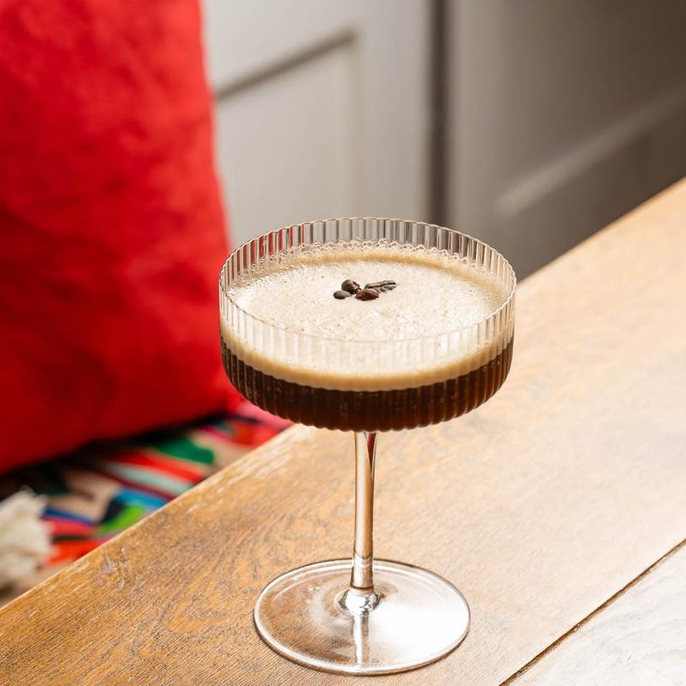 Espresso martini in a ribbed coupe glass, garnished with coffee beans on a wooden table.
