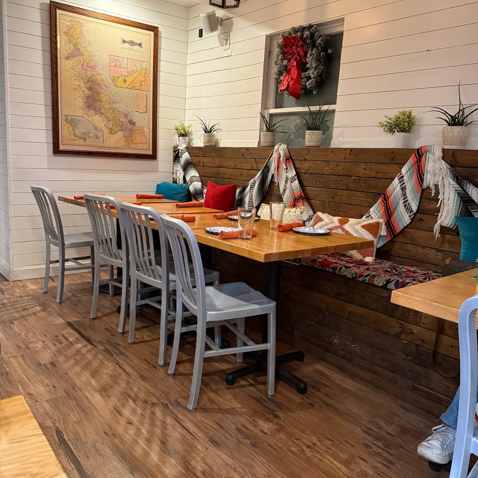 Restaurant interior with wooden tables, gray chairs, a map on the wall, and festive holiday decorations.